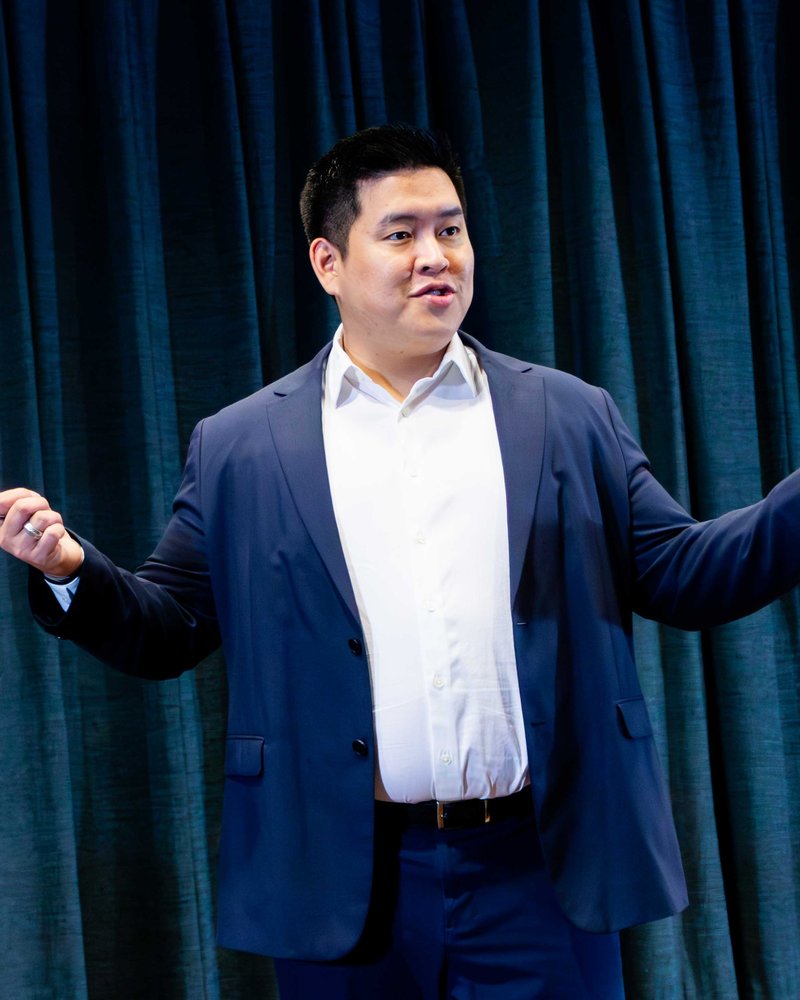 John Weng mid-presentation, gesturing, indirect gaze — caught teaching.